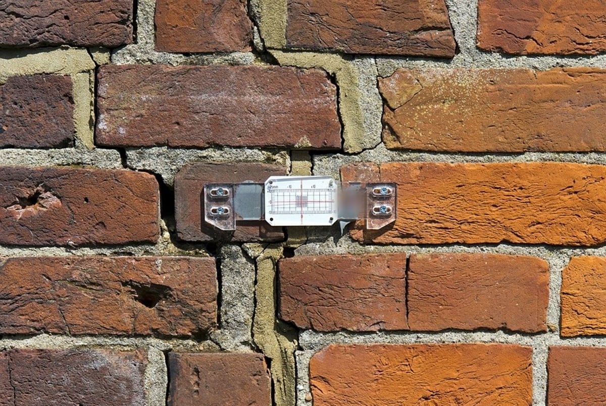 Rissmonitor mit Millimeterskala, verschraubt über einem Riss in einer Klinkerwand