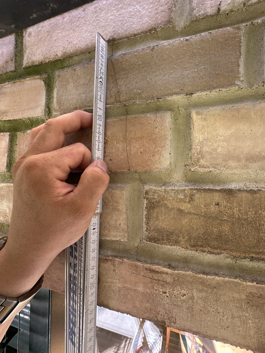 Zollstock senkrecht an einem Riss, der über 3 Steinlagen einer Klinkerfassade läuft